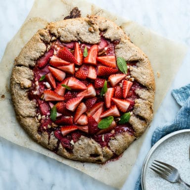 A whole fresh galette on parchment paper ready to be served with a fork and plate and blue napkin off to the side