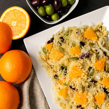 A platter of couscous arranged with oranges off to the side and a bowl of olives on top