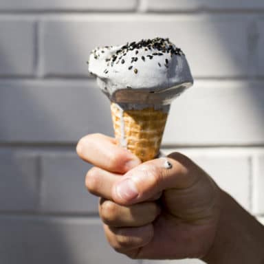 A hand holding a melting cone of black sesame ice cream