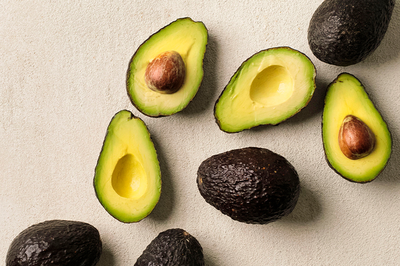 Avocados artfully arranged, some halved with the pit showing, some pitted, some whole