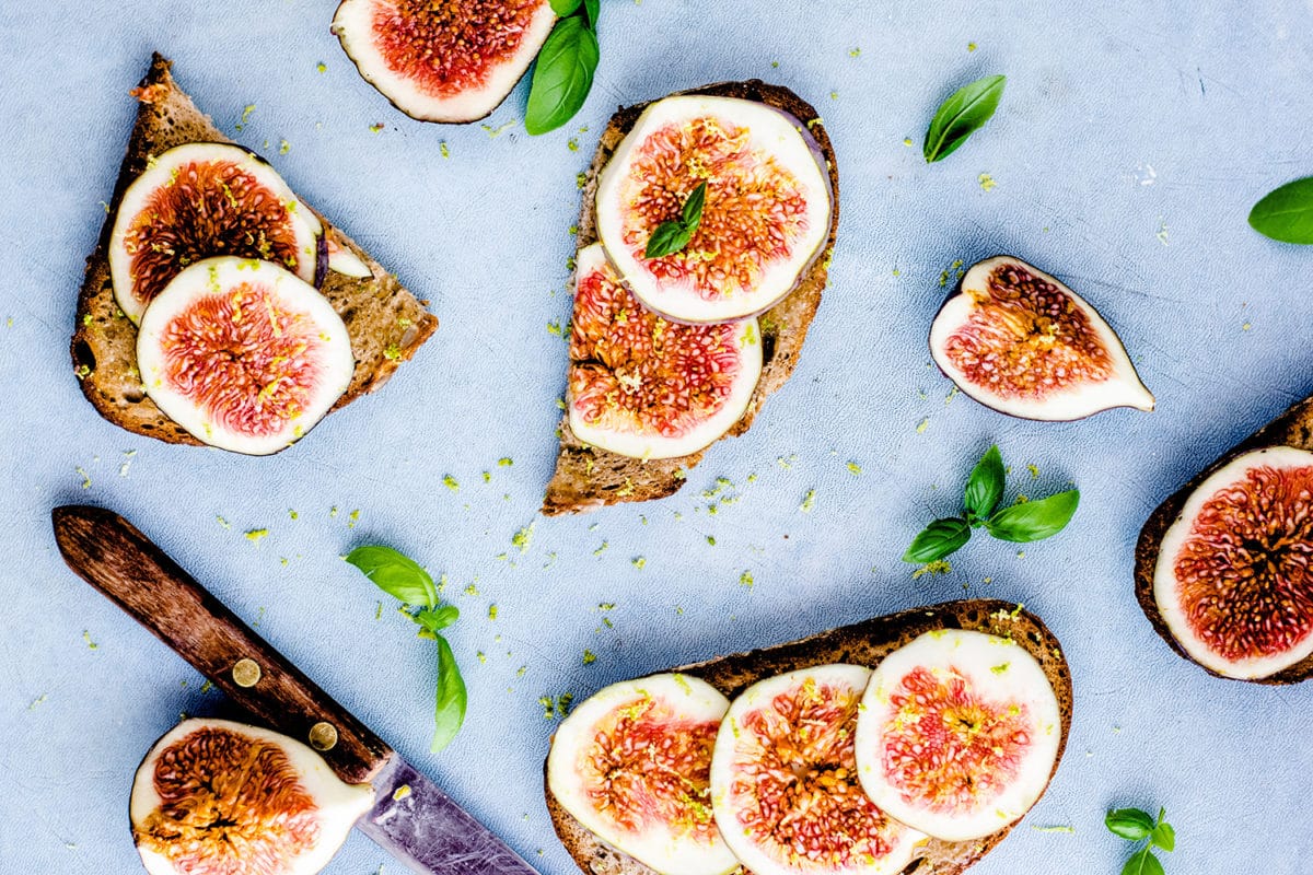 Toast slices with slivers of fresh figs on them and herbs around them