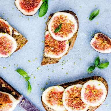 Toast slices with slivers of fresh figs on them and herbs around them