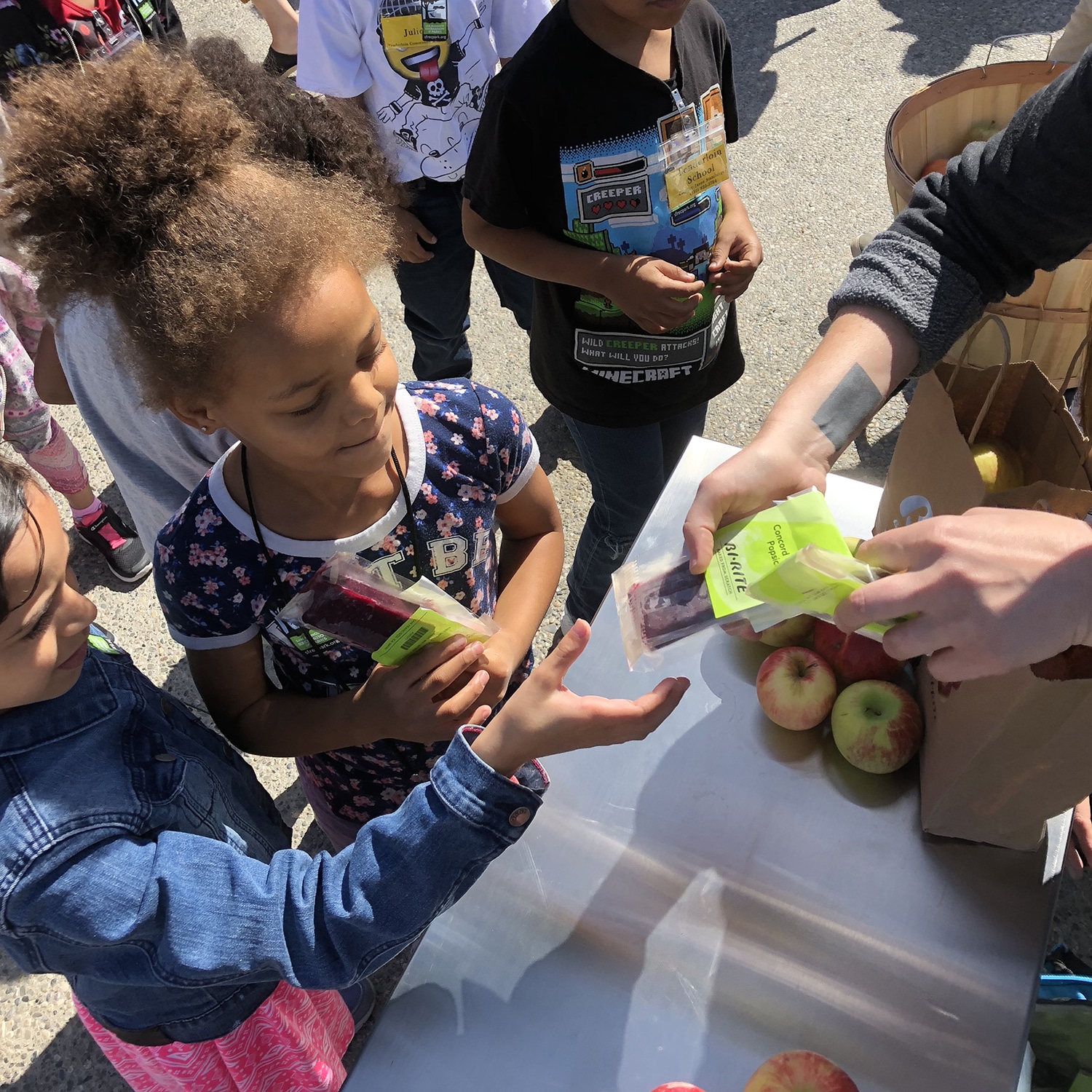 Children lining up, one receiving an ice pop and apples