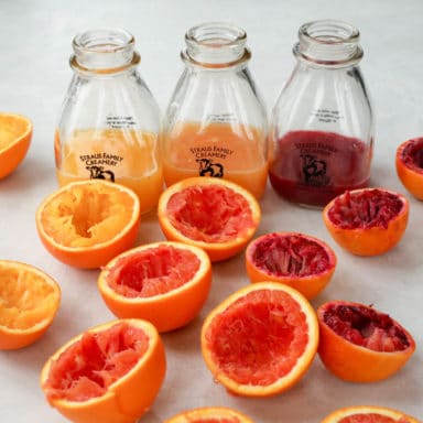 Juiced remains of citrus with three juice bottles in the background