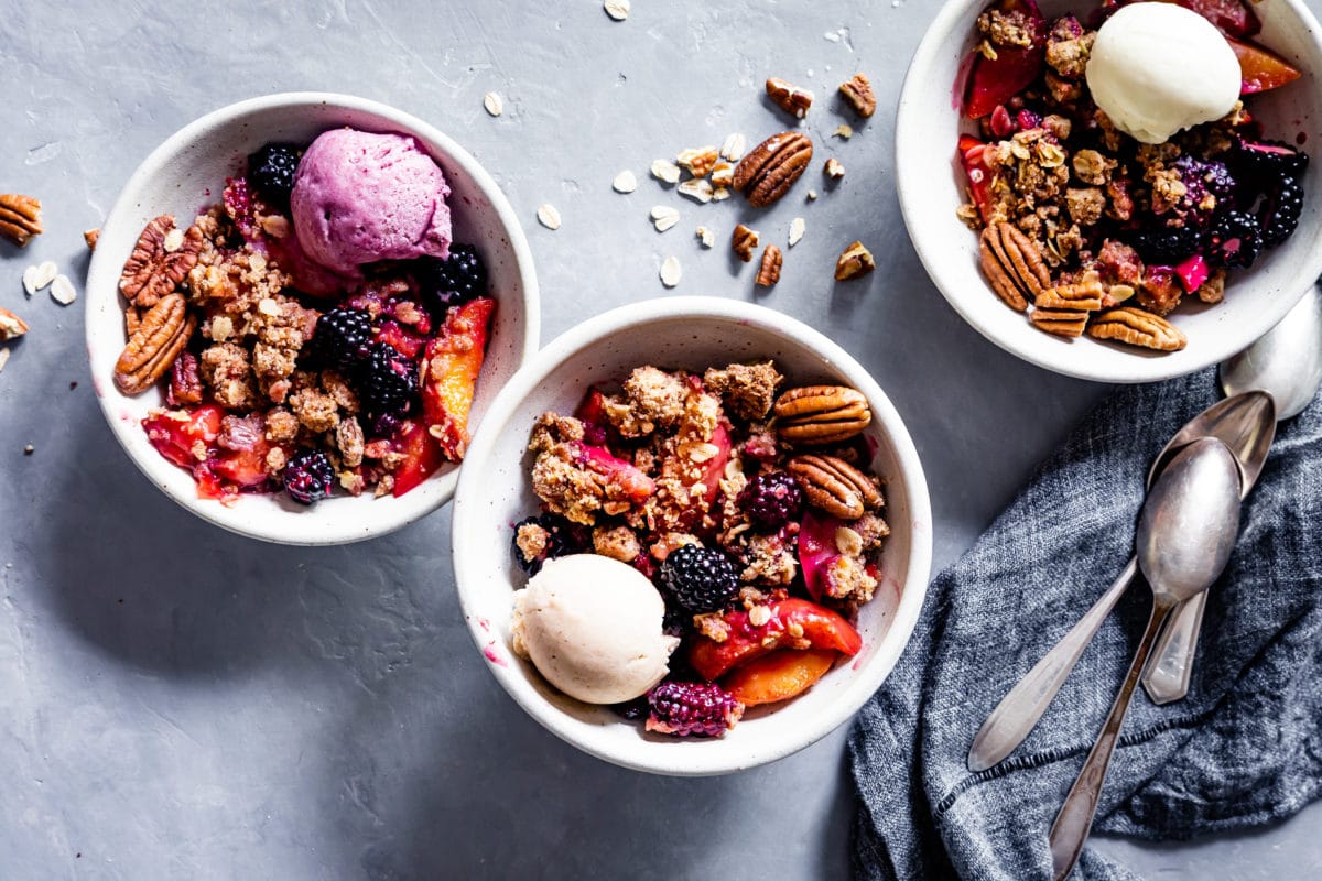 Three bowls of blackberry peach crisp and a spoon and napkin