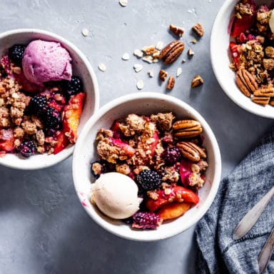 Three bowls of blackberry peach crisp and a spoon and napkin