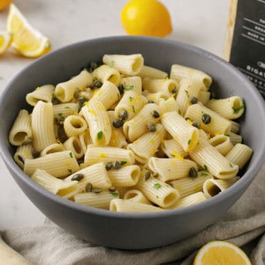 A bowl of rigatoni with herbs and lemon wedges