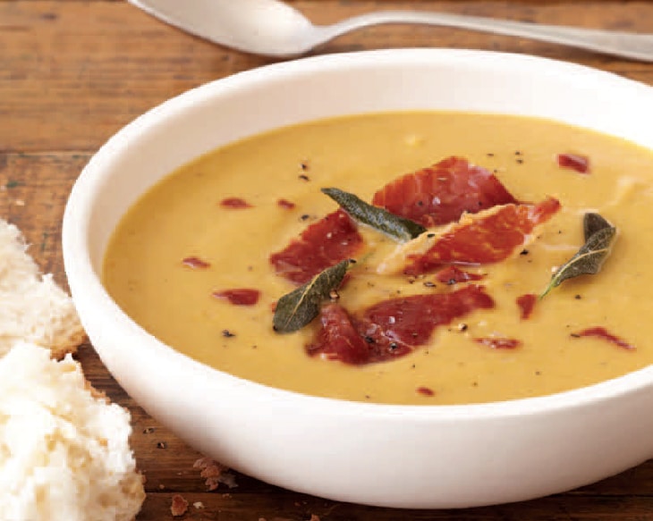 A bowl of the puree with prosciutto pieces and a spoon and crust of bread