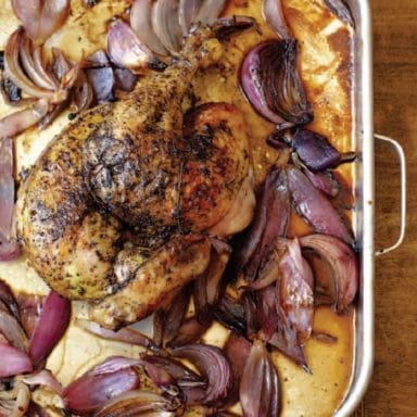 A roasted chicken in the middle of cut onions in a baking dish