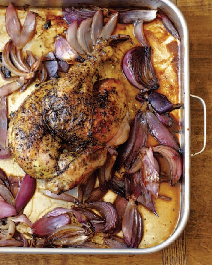 A roasted chicken in the middle of cut onions in a baking dish