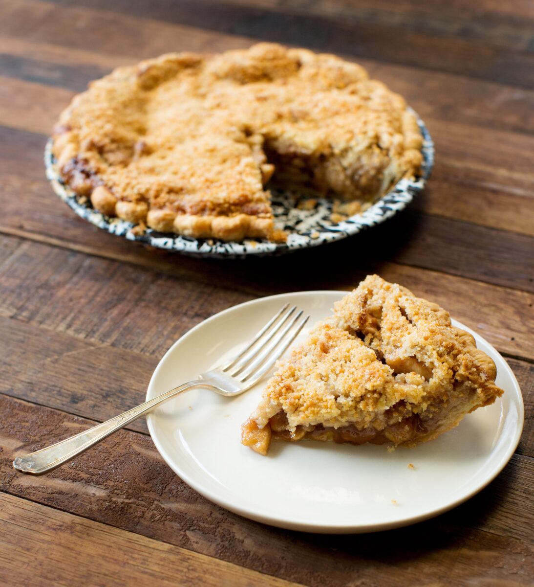 A plated slice of apple pie with a whole pie in the background