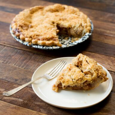 A plated slice of apple pie with a whole pie in the background