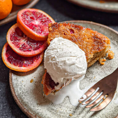 A slice of orange cardamom cake served a la mode with blood orange wheels to the side