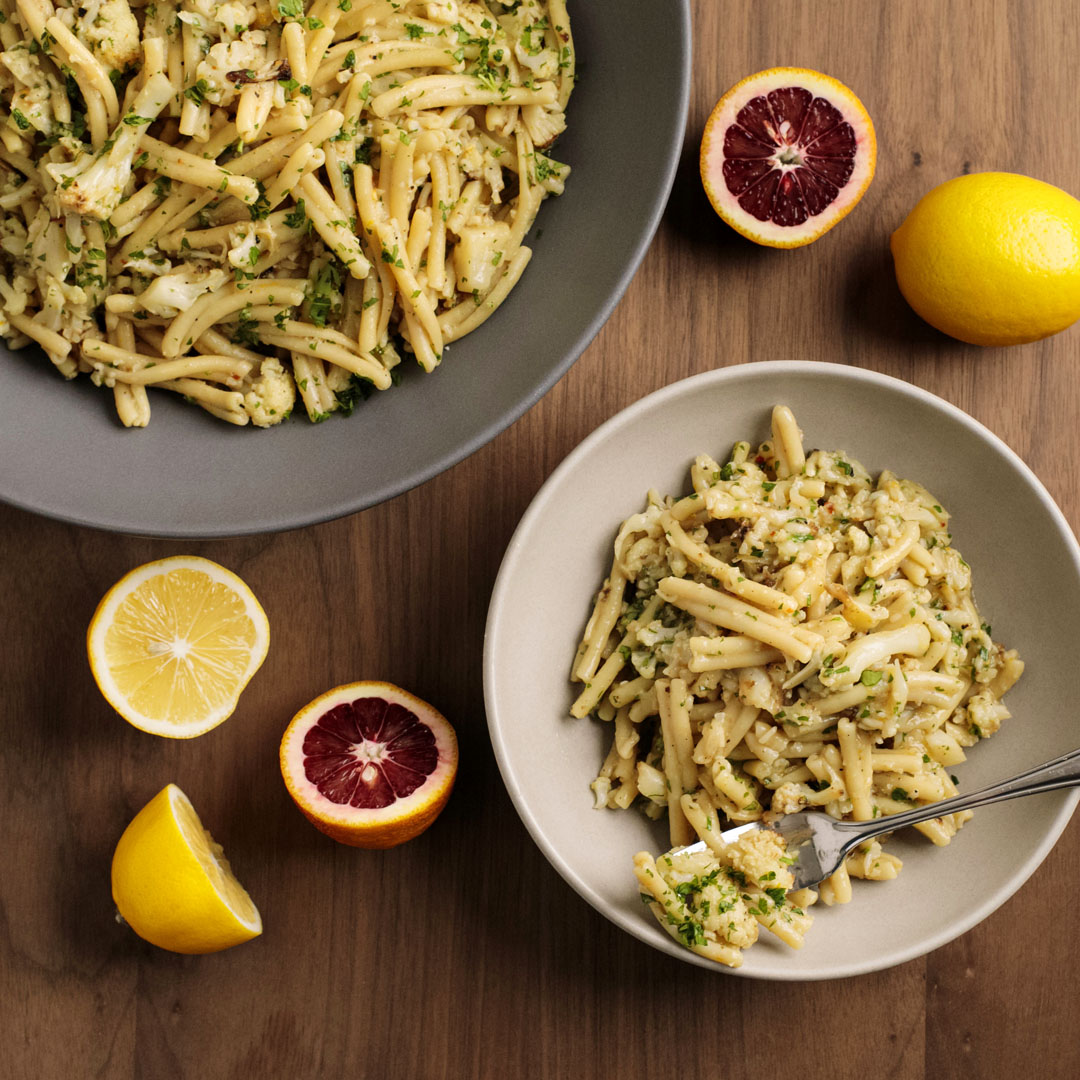 Two bowls of pasta, one large and one small, with halves of citrus next to each other