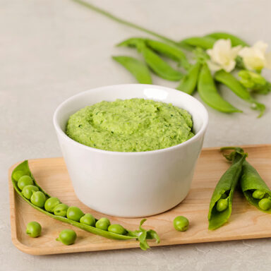 A bowl of spring pea hummus with a pod of peas and blossoms
