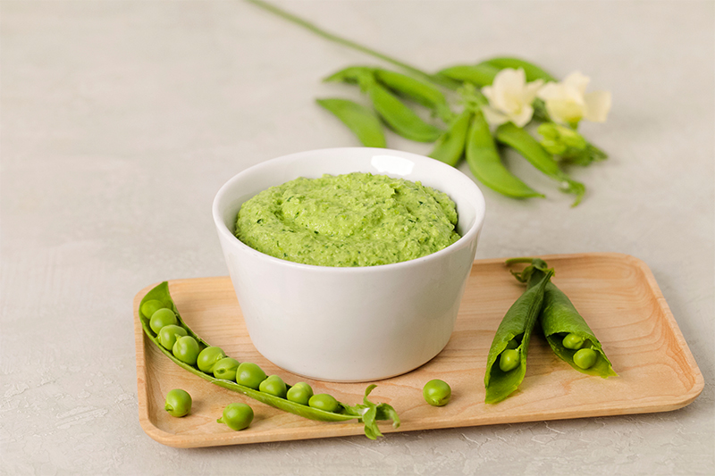 A bowl of spring pea hummus with a pod of peas and blossoms