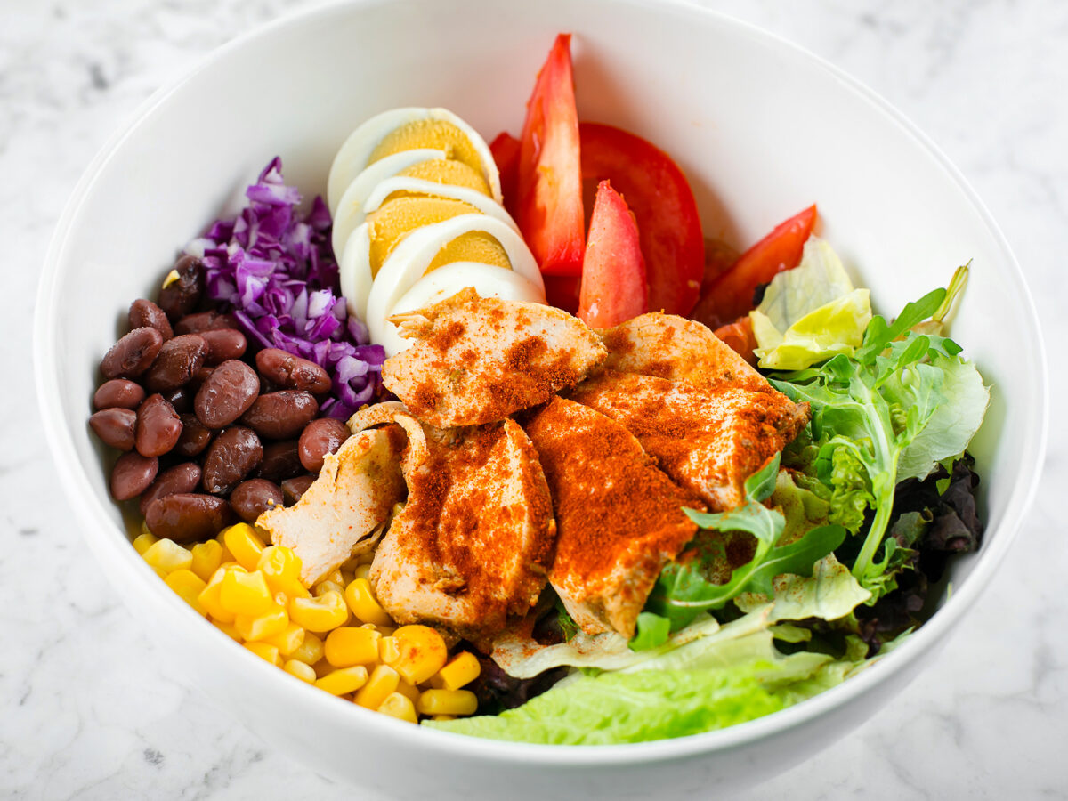 A bowl of beans, corn, boiled egg slices, greeans and chicken