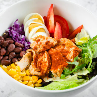 A bowl of beans, corn, boiled egg slices, greeans and chicken
