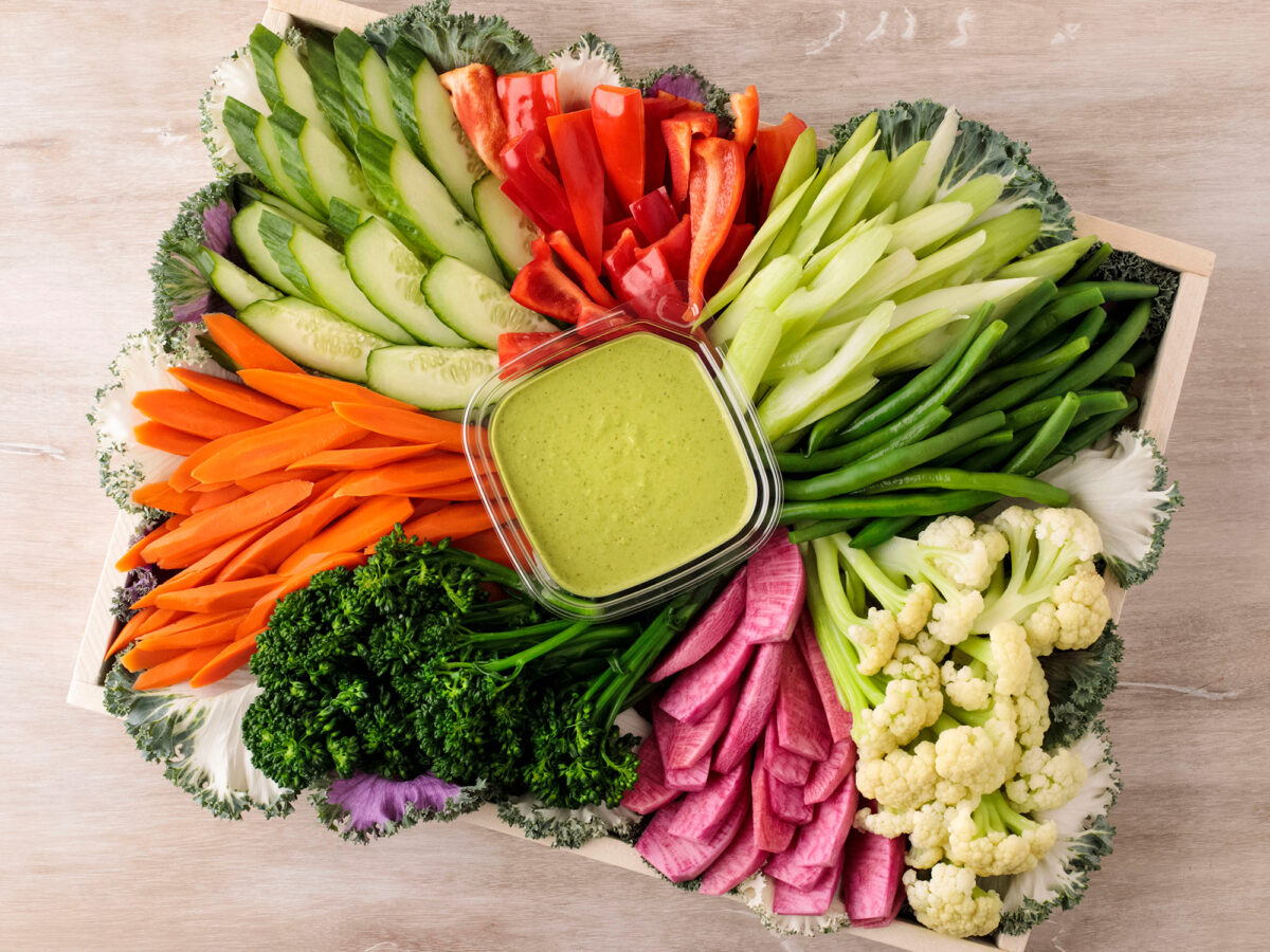 A crudite platter with a variety of julienned vegetables with green goddess dressing in the middle