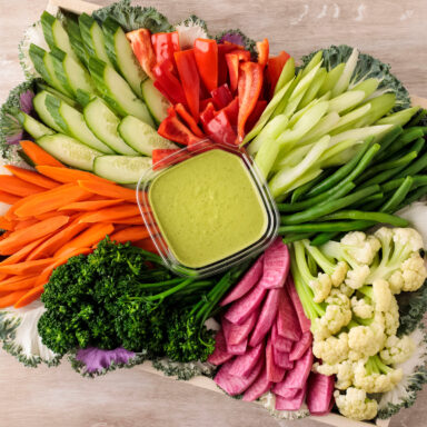 A crudite platter with a variety of julienned vegetables with green goddess dressing in the middle