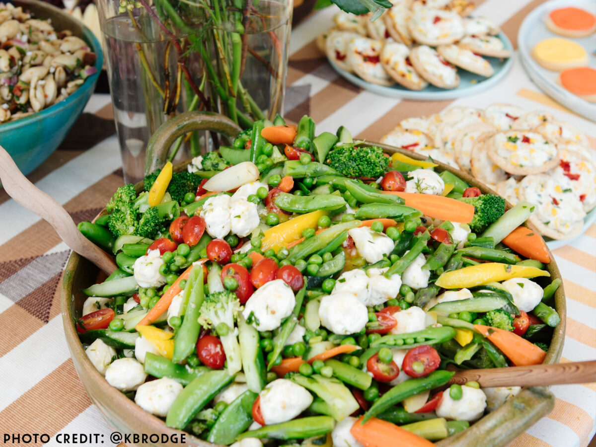 A bountiful salad with lots of fresh spring vegetables including peas, tomatoes and fresh cheeses on a table with florals