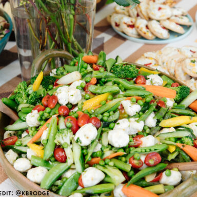A bountiful salad with lots of fresh spring vegetables including peas, tomatoes and fresh cheeses on a table with florals