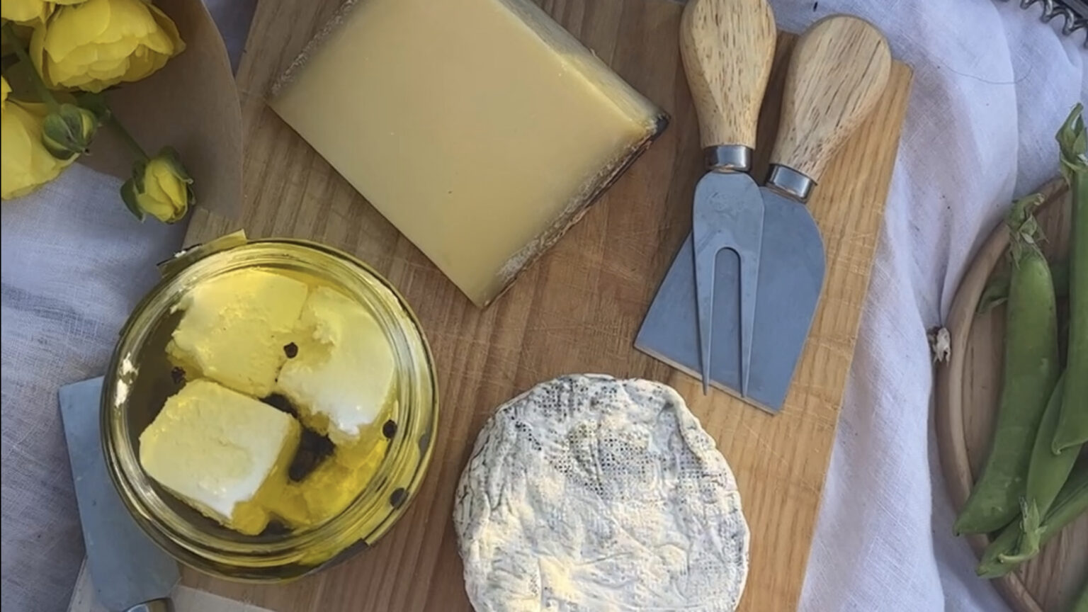 A cheese board with soft, hard and fresh cheeses, with flowers and snap peas at edge of frame