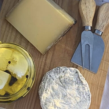 A cheese board with soft, hard and fresh cheeses, with flowers and snap peas at edge of frame