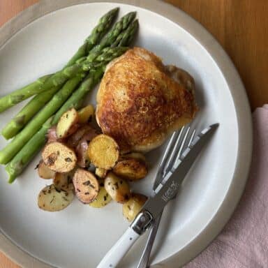 Plate of panfried chicken thighs, new potatoes with herbs and a side of asparagus.