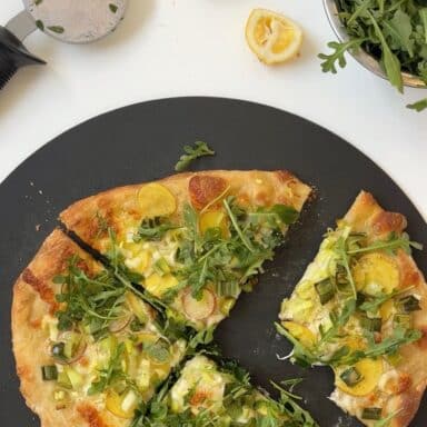 Homemade pizza with potatoes, leeks, and green garlic, topped with fresh arugula.