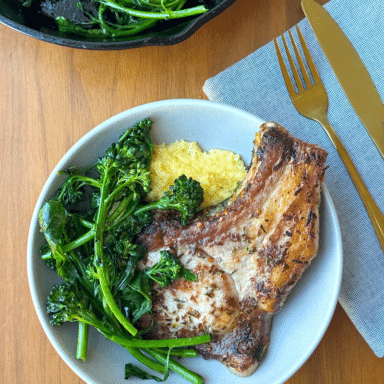 A shallow bowl filled with polenta and a big pork chop, with a pile of broccoli on the side.