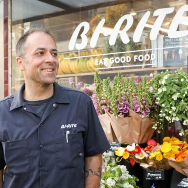 Sam standing and smiling in front of the Bi-Rite storefront, backed by bouquets of flowers.