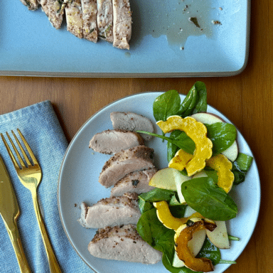 A white plate with sliced pork tenderloin fanned on one side, and a tangle of squash and apple salad on the other.