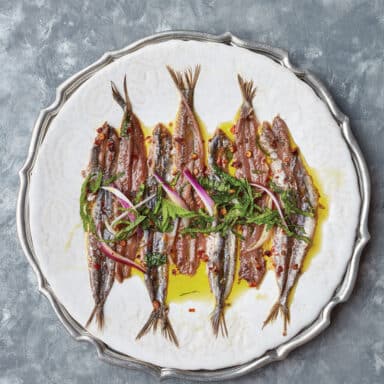 A Plate Of Artfully Arranged Anchovies, Drizzled With Olive Oil, And Scattered With Slivered Red Onions And Fresh Herbs