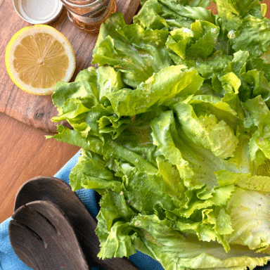 A Large Bowl Overflowing With Frilly Escarole Leaves, With Anchovies, Half A Lemon, And Tongs Ready Nearby