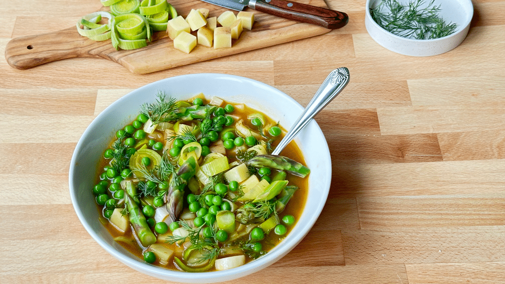 A Bowl Of Spring Celebration Veggie Soup On A Wooden Surface With A Cutting Board Of Peas And Potatoes And A Dish Off Fresh Dill In The Background