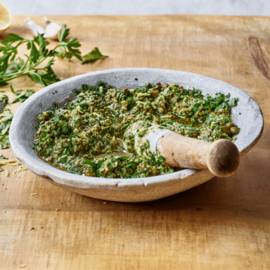 Salsa Verde In A Morter And Pestle With Cilantro Lemon Garlic In The Background
