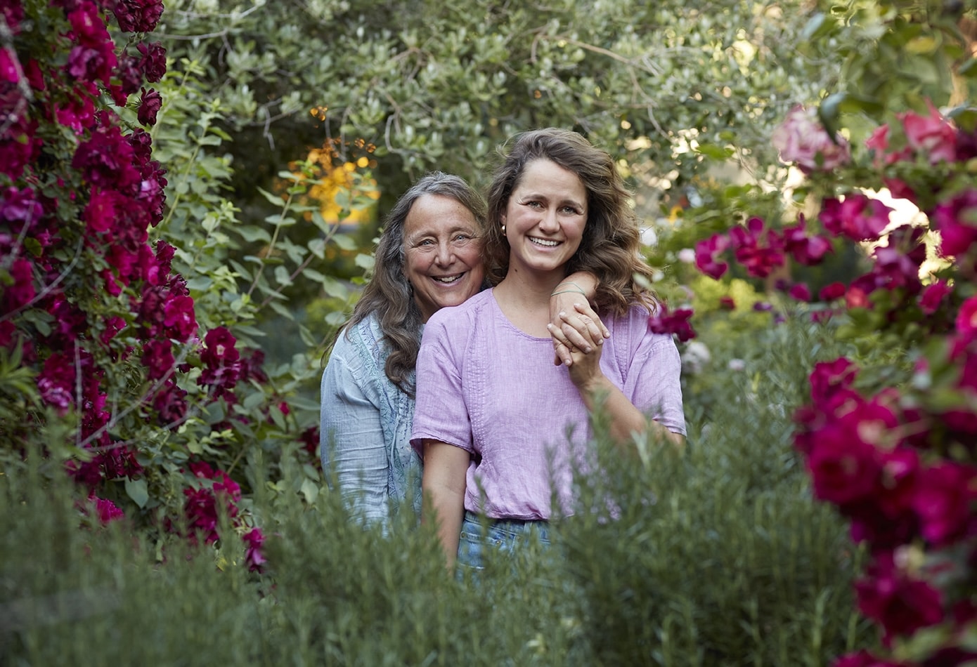 Dru Rivers and Hannah Muller of Full Belly Farm, facing the camera, Dru's arm draped across Hannah amongst a lush canopy of flowers