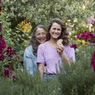 Dru Rivers and Hannah Muller of Full Belly Farm, facing the camera, Dru's arm draped across Hannah amongst a lush canopy of flowers