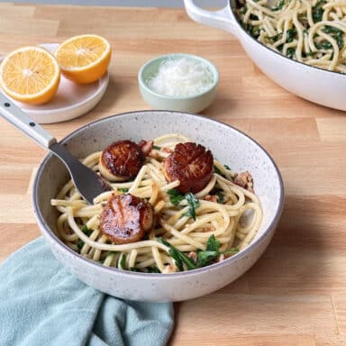 a bowl of scallop pasta with cut citrus, salt and a napkin to the side