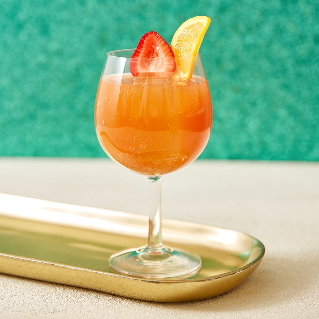 A bourbon cocktail with a green background on a gold tray