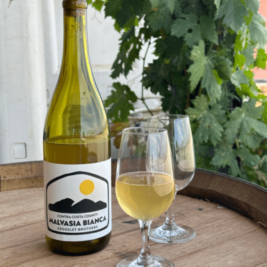 A Bottle And Two Glasses Of Erggelet Brothers Malvasia Bianca On A Table Outdoors