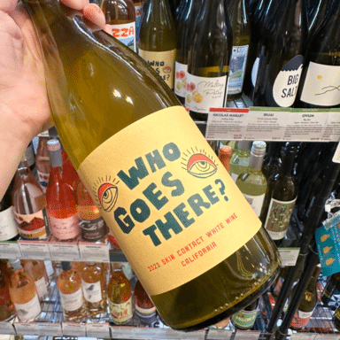 Hand Holding A Bottle Of En Cavale Who Goes There In From Of Other Wine Bottles