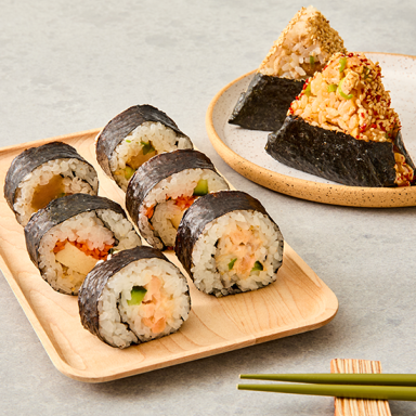 6 Rolls Sushi On Plate Next To 2 Onigiri And Chopsticks On Grey