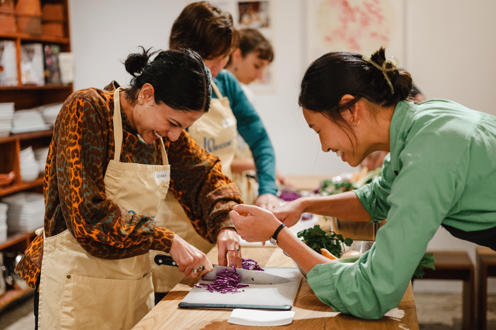 Instructor helps a student chop vegetables during an 18 Reasons cooking class