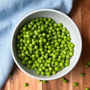 Bowl Of Peas With Scattered Peas On Wood With Blue Napkin Cutting Down Center