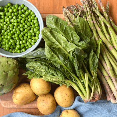 Mis En Place Of Bowl Of Peas Artichoke Golden Potatoes Bunch Of Lettuce Bunch Of Asparagus On Wood Cutting Board With Blue Napkin
