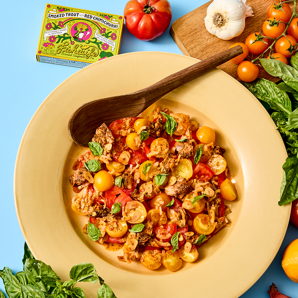 Plated Tinned Fish Tomato Salad In Yellow Plate On Blue Background Surrounded By Garlic Tomatoes Cutting Board Basil