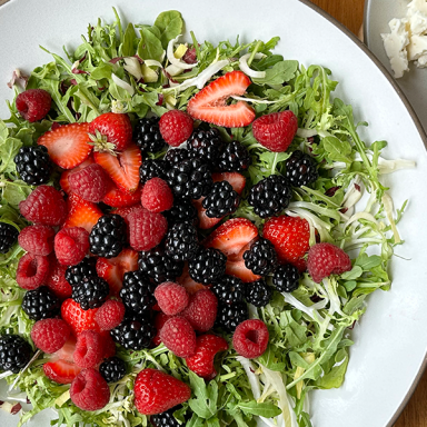 Summer Berry Salad Plated With Frisee And Chese And Almonds And Dressing On The Right Side With Blue Napkin And Tongs